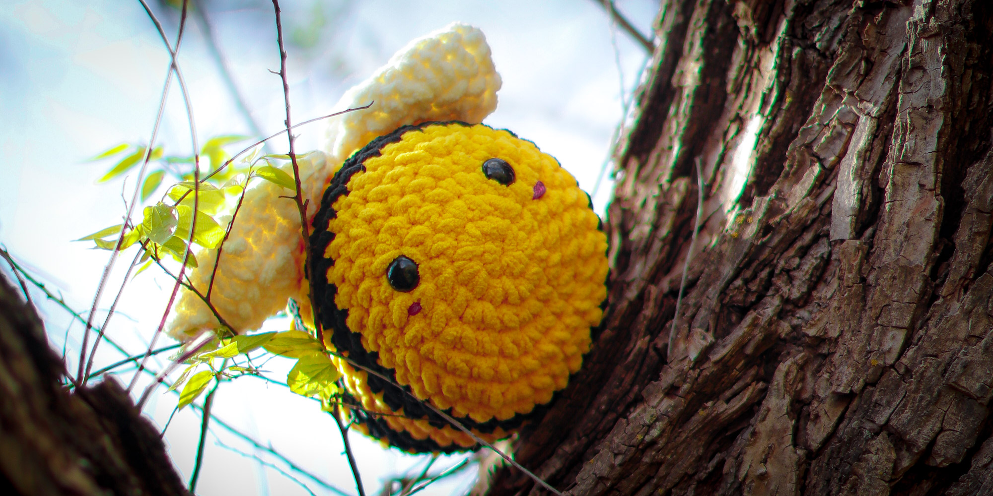 A single yellow bee perches atop a willow tree. These bulbous bees have a softness to the touch which customers rave about, yet justaposing them against the hard bark of nature both emphasizes how the product reflects the natural world, and how it contains a softness often lacking there.